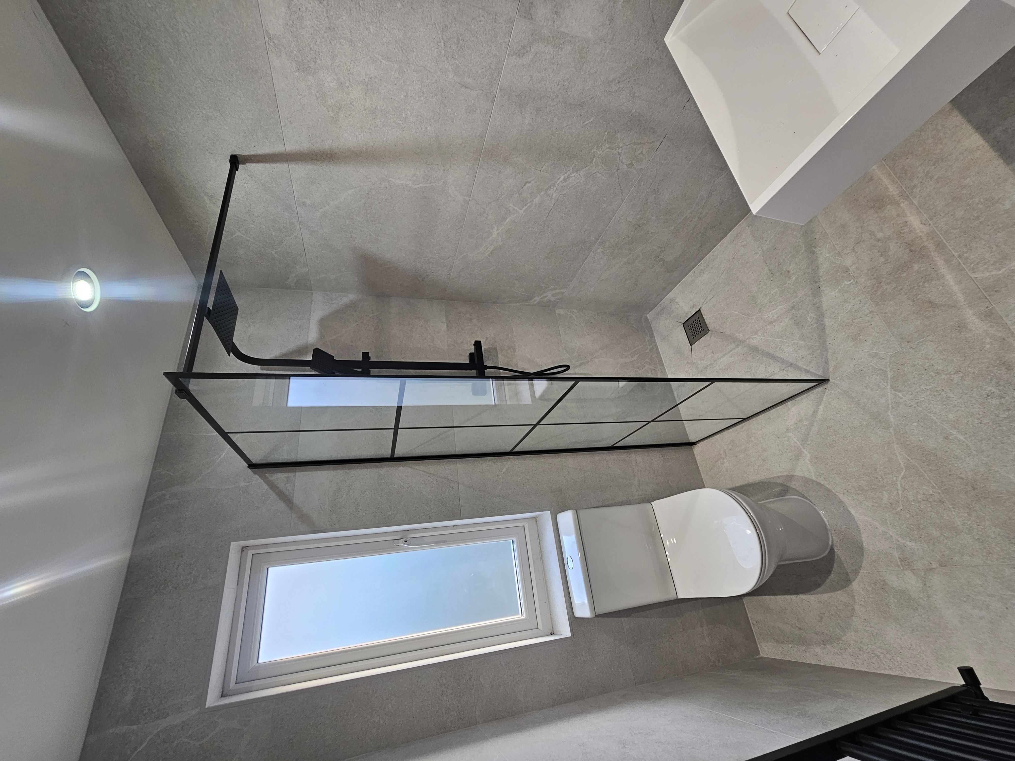Grey tiled bathroom with black framed walk-in shower and rainfall head