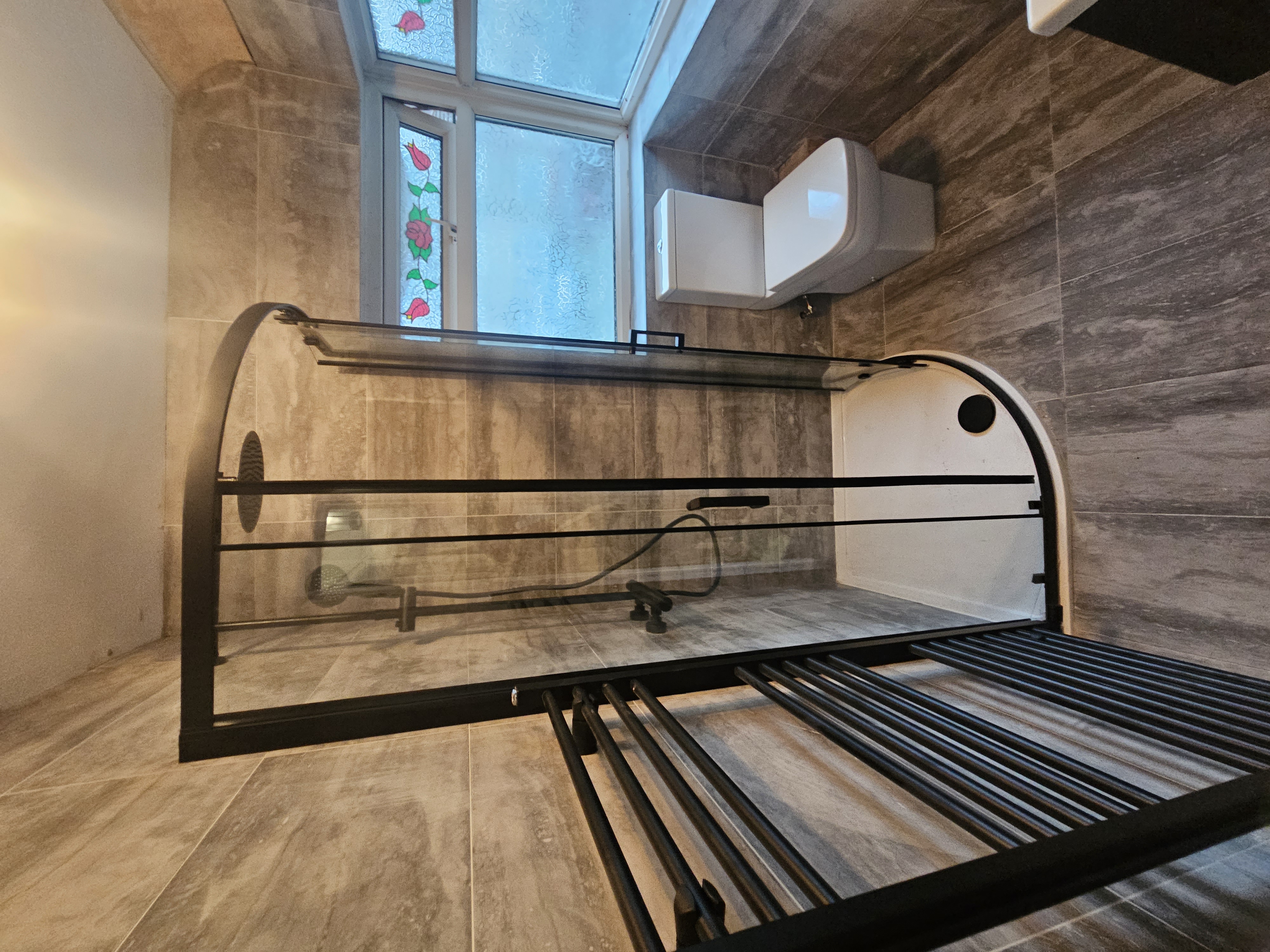 Warm stone-effect bathroom with curved black framed shower enclosure