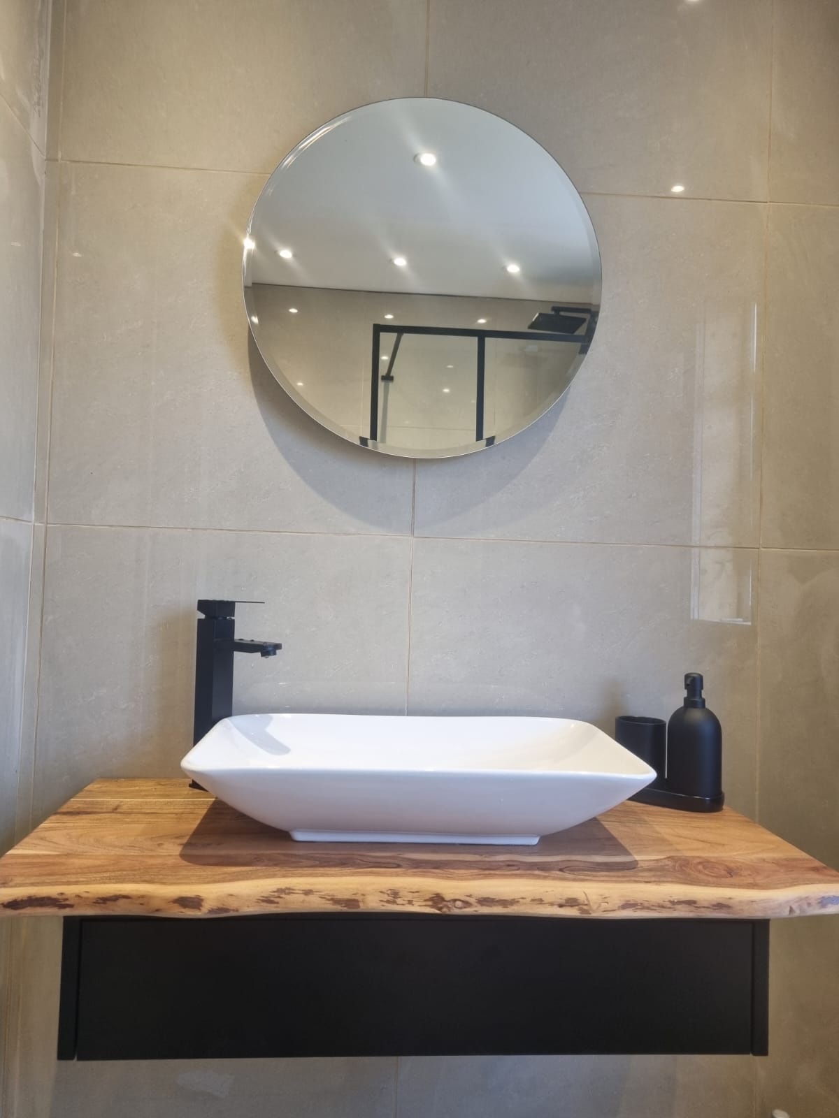 Floating timber vanity with countertop basin, round mirror and black brassware